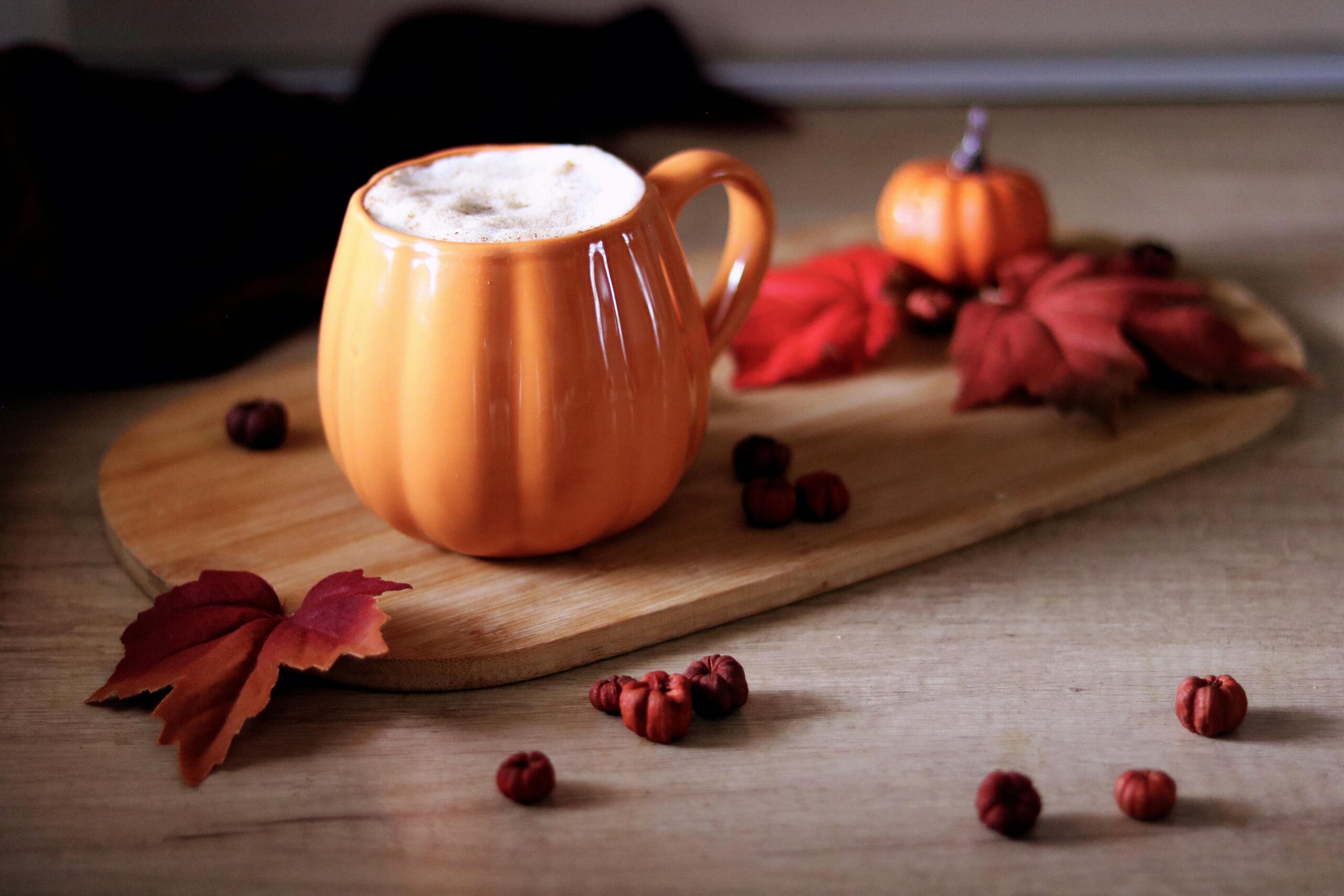 Warm and cozy autumn scene with pumpkin-shaped mug and latte on a wooden board.